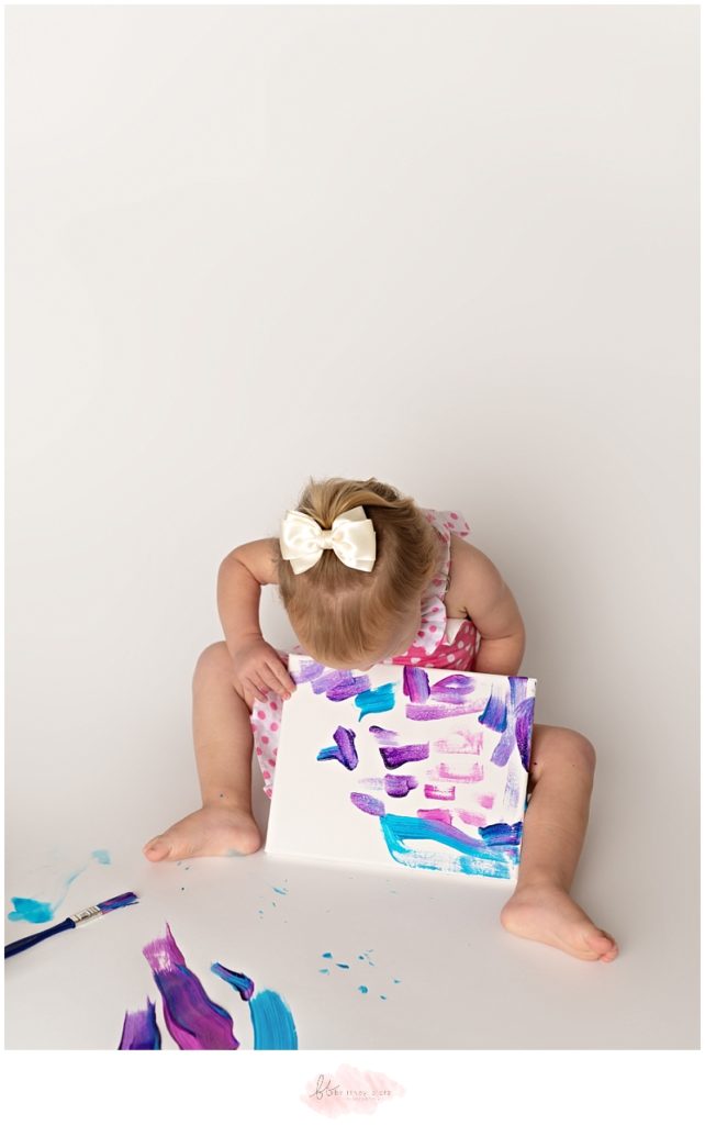 2-year old girl in pink, polka dot apron showing off her painting masterpiece